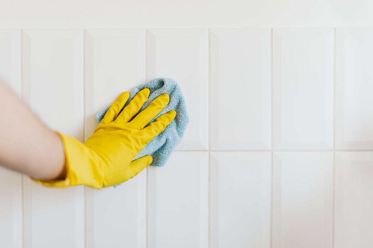 mold vs mildew - rubber gloved hand cleaning a tiled surface