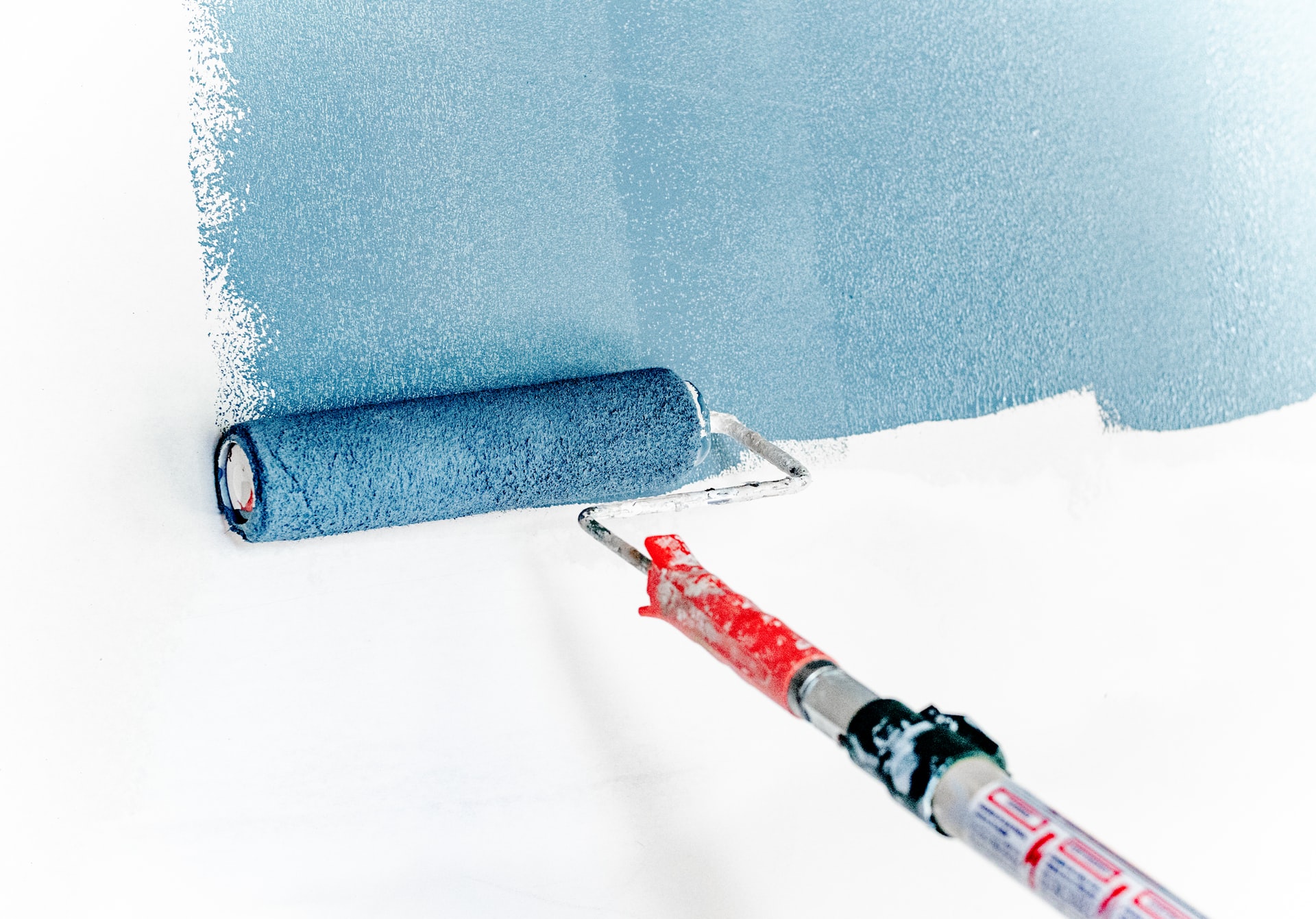 mold resistant paint -- paint roller brush in the middle of paining a white wall with blue paint
